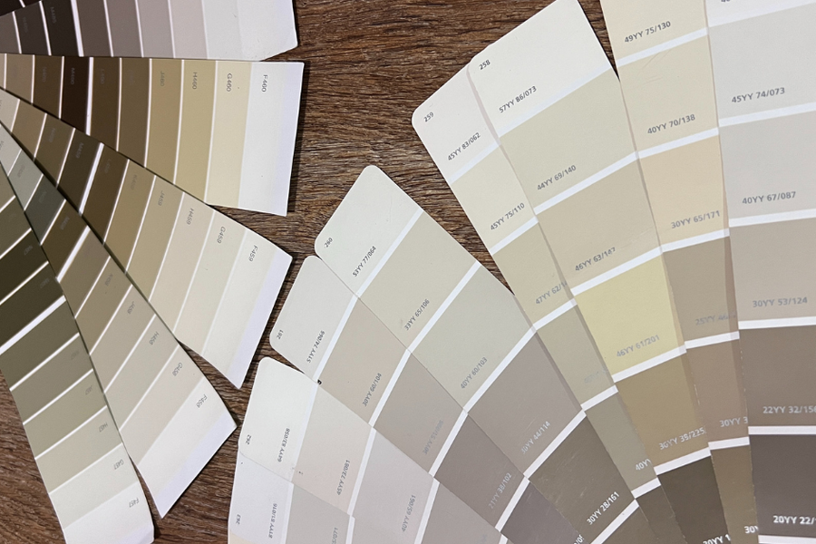 Several paint color fan decks spread across a wooden table, fanned open to swatches in neutral shades of cream, beige, taupe, and gray.