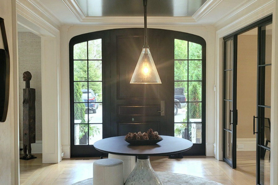 Entry foyer with a dark arched front door flanked by paned windows, a glass pendant light over a round black table, and cream walls with white trim.