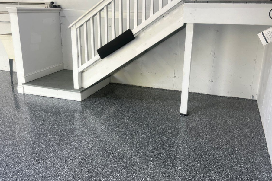 Garage interior with a speckled gray epoxy-coated floor, white walls, and a white staircase with a landing in the corner.