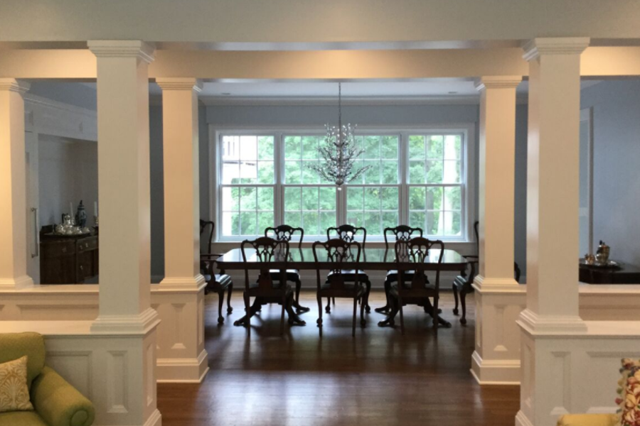Formal dining room framed by white square columns and paneled half walls, with a mahogany table and chairs, a chandelier, and pale blue walls around large windows.