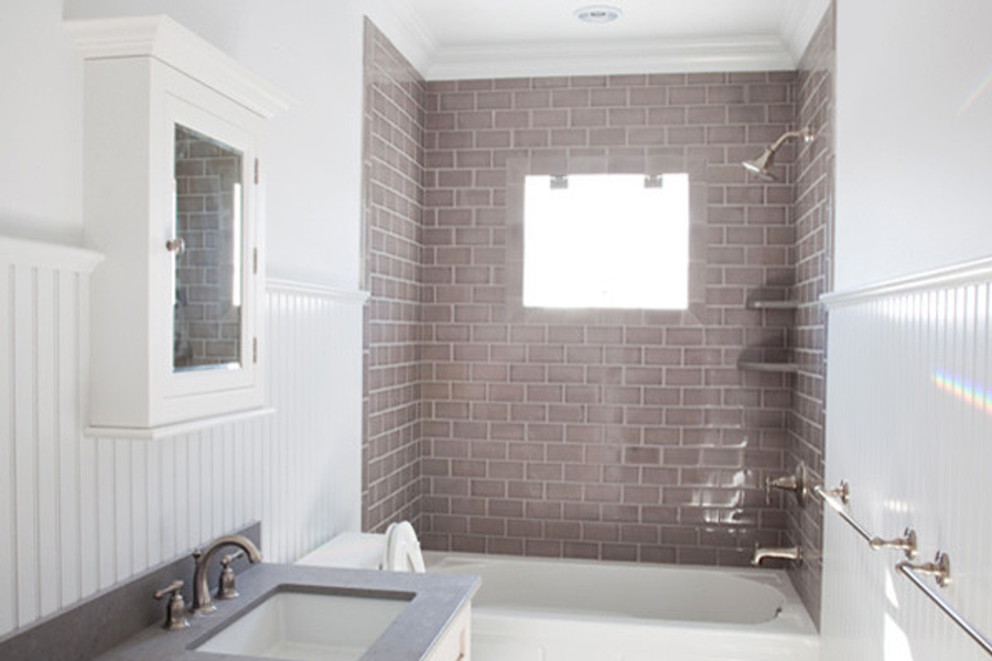 Renovated bathroom with white beadboard wainscoting, taupe subway tile around the tub and shower, a gray vanity countertop, and a window above the tub.