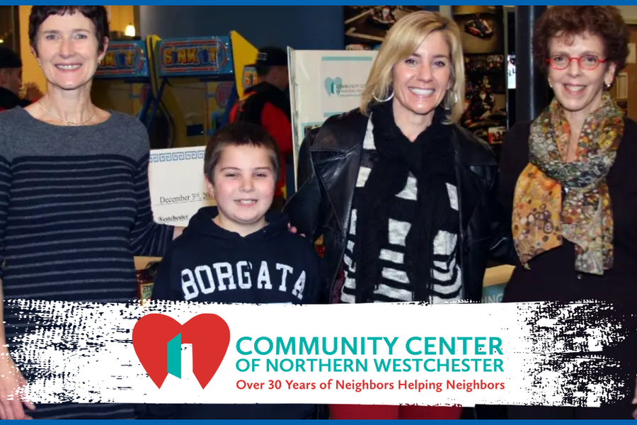 Three women and a boy stand beside boxes of donated food at an indoor event, above a Community Center of Northern Westchester logo reading "Over 30 Years of Neighbors Helping Neighbors."