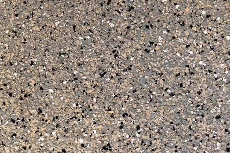 Close-up of a decorative flake floor coating with tan, gray, black, and white chips scattered densely across the surface.