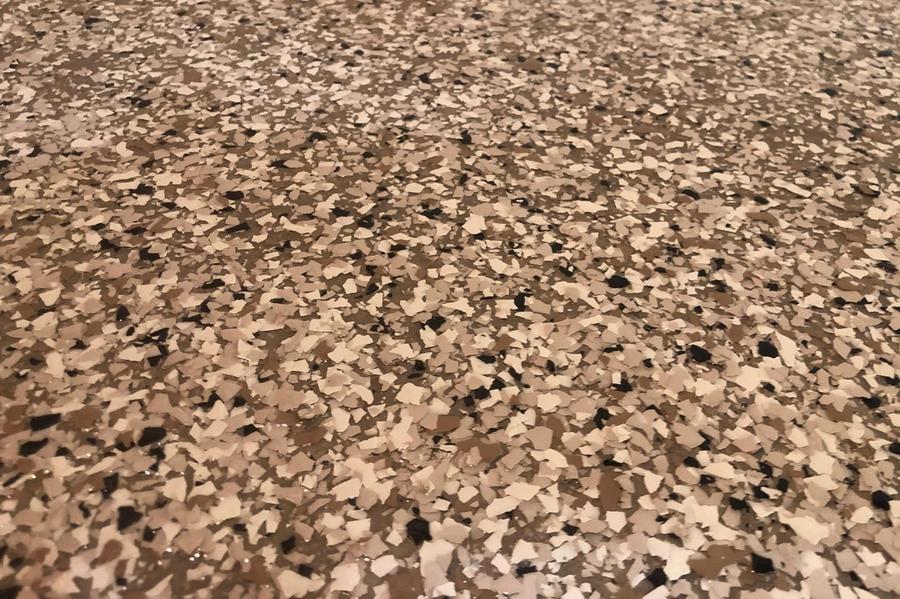 Close-up of a finished floor coating with black, white, tan, and gray decorative flakes set in a glossy epoxy surface.