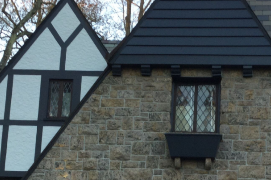 Tudor-style home exterior with a stone facade, white stucco gable with dark half-timbering, leaded diamond-pane windows, and a black window box.