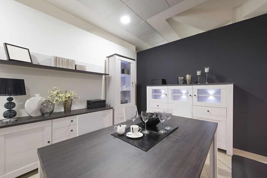 Modern dining room with a dark charcoal accent wall, white cabinetry, a gray wood table set with glassware, and black decorative accessories.