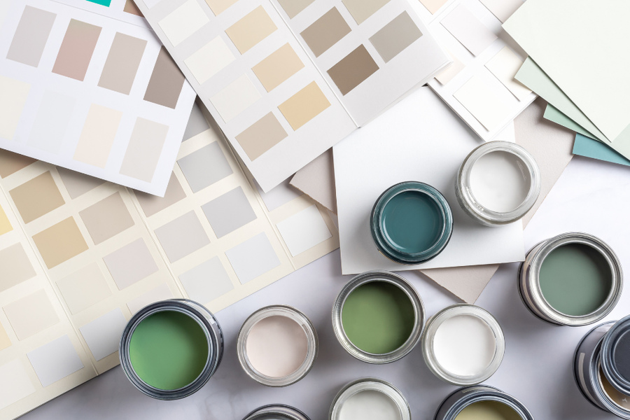Overhead view of open paint sample cans in greens, teal, white, and cream arranged among fanned color swatch cards and paint chip sheets.