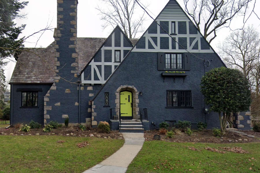 Tudor-style home painted dark blue-gray with light half-timber accents, stone trim, and a bright chartreuse front door at the end of a walkway.