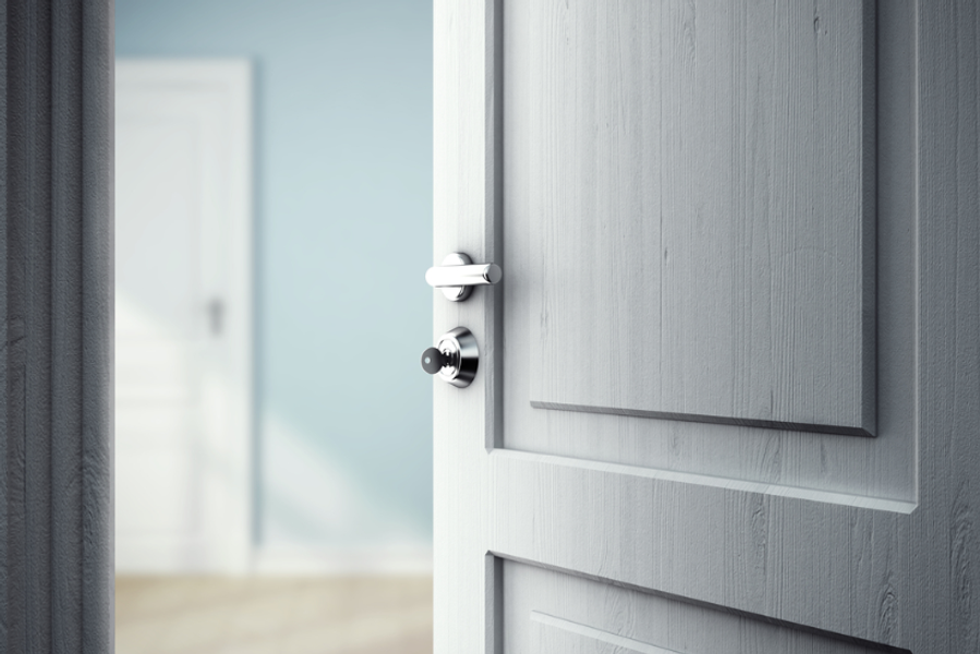 Close-up of a light gray painted panel door slightly ajar, showing a chrome lever handle and lock, with a soft blue wall blurred in the background.