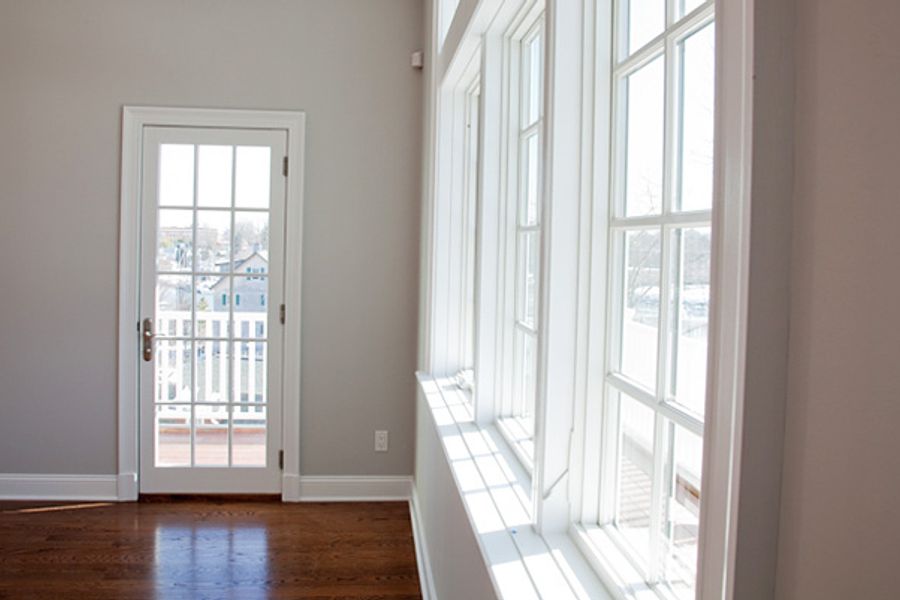 Sunlit room with light gray walls, white-trimmed multi-pane windows, a glass-paned door opening to a balcony, and polished hardwood floors.