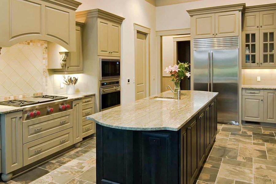 Spacious kitchen with sage-green painted cabinets, a dark center island topped with granite, stainless steel appliances, and slate tile flooring.