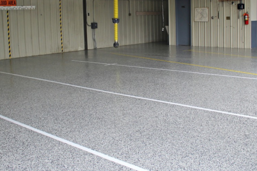 Speckled gray epoxy-coated floor with painted white and yellow line markings inside a commercial garage bay, with metal walls and a small "Flood Area" sign.