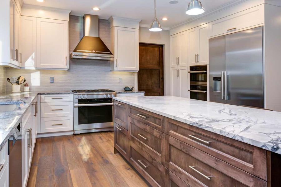 Remodeled kitchen with white painted cabinets, a wood-stained island topped with marble, stainless steel appliances, and hardwood flooring.