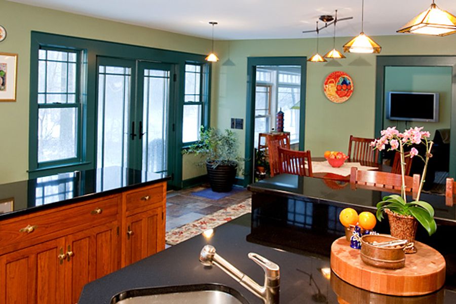 Kitchen with sage green walls, dark teal window trim, wood cabinets, black countertops, pendant lights, and a potted orchid beside a butcher block near the sink.