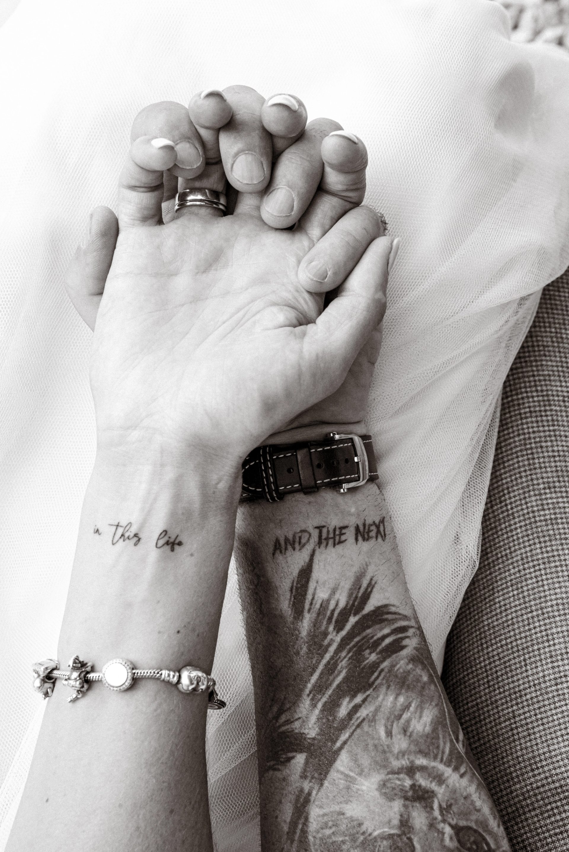 Maren und Ralph halten sich an den Händen, Eheringe, Armband und Tätowierungen am Handgelenk, schwarz-weiß