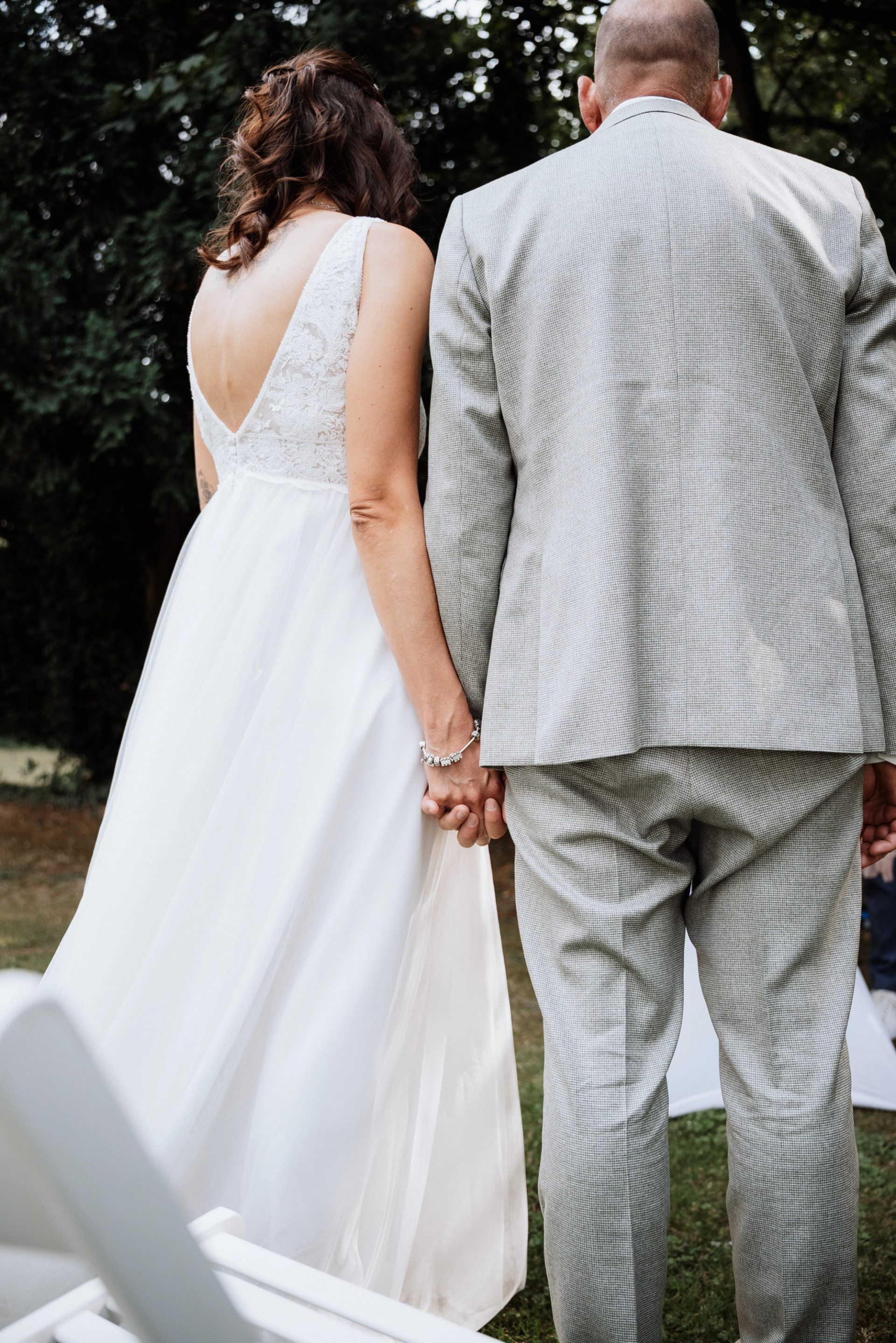 Maren und Ralph stehen im Garten Hand in Hand, von hinten gesehen