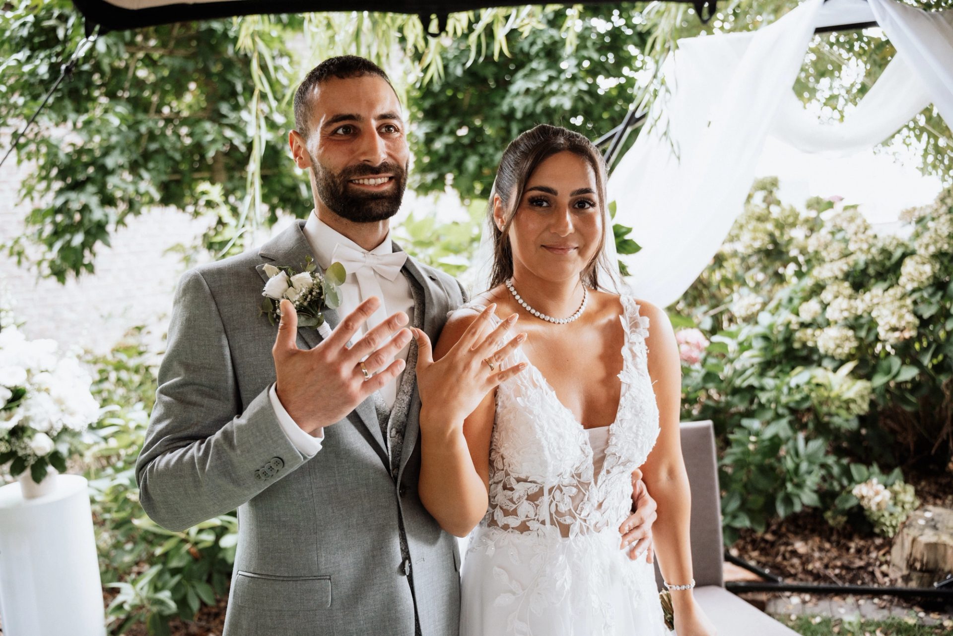 Merve und Timur zeigen lächelnd ihre Hände mit den Ringen