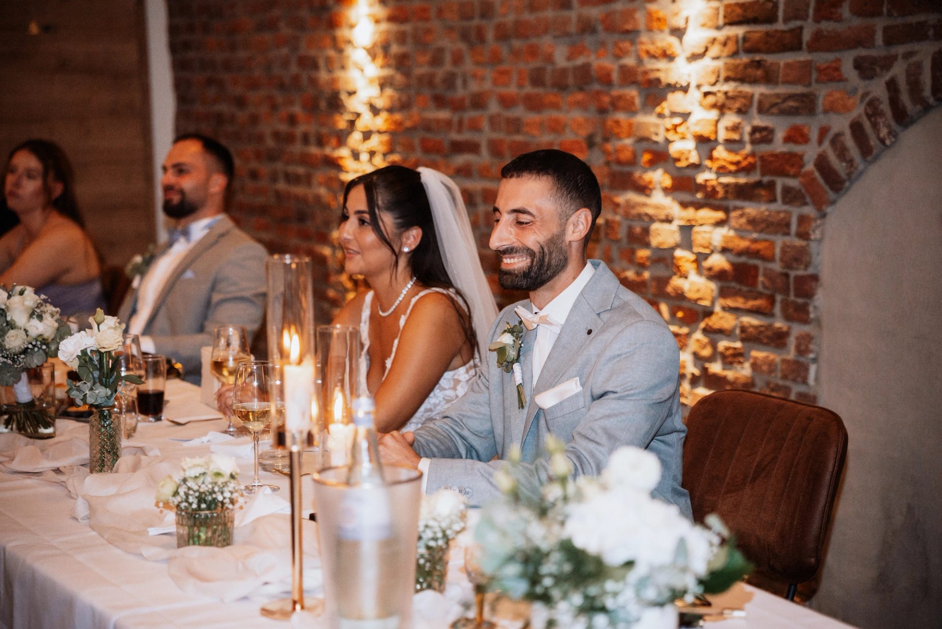Merve und Timur lachen am Brauttisch vor der Backsteinwand