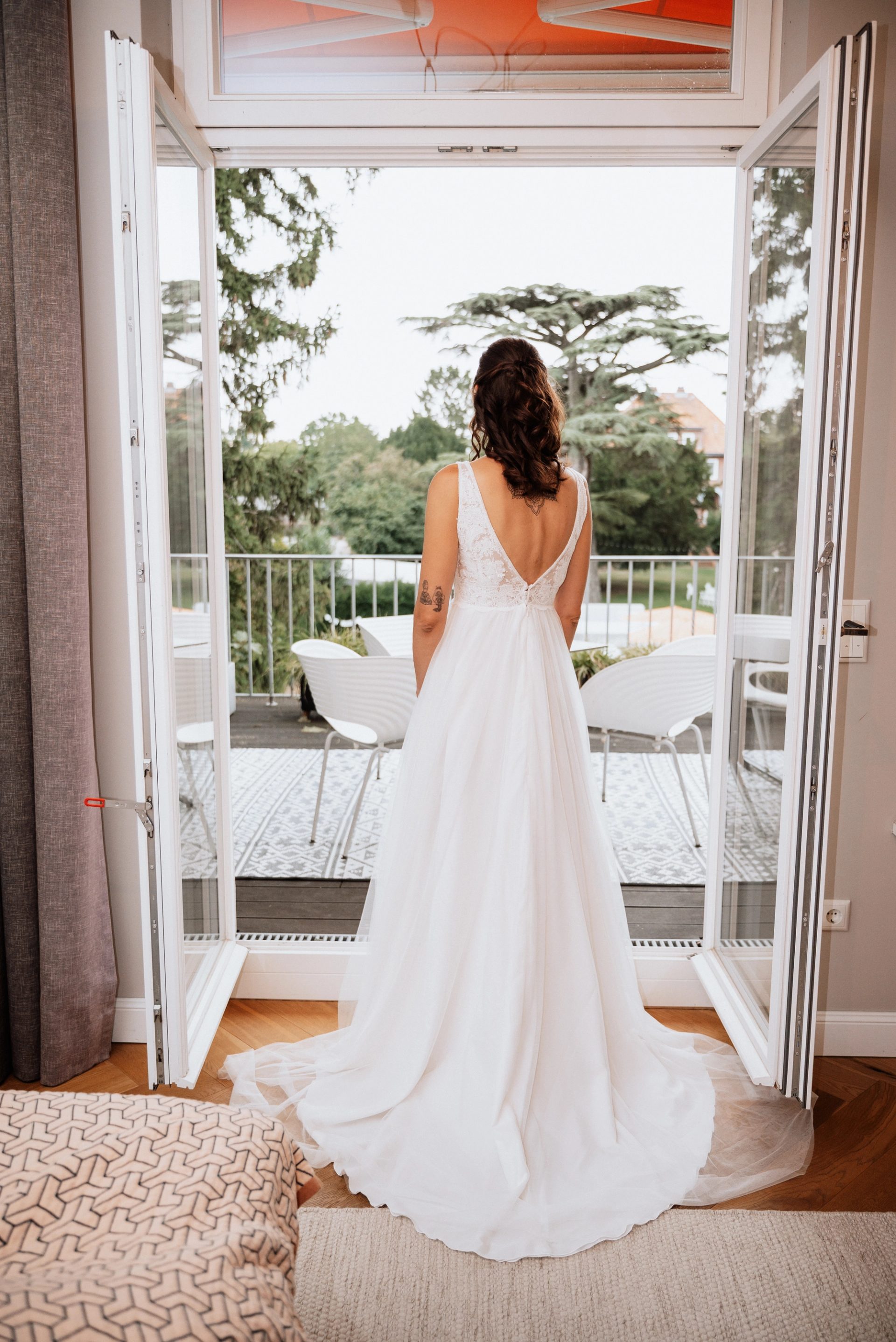 Maren im Brautkleid von hinten in der offenen Balkontür, die Schleppe liegt auf dem Boden