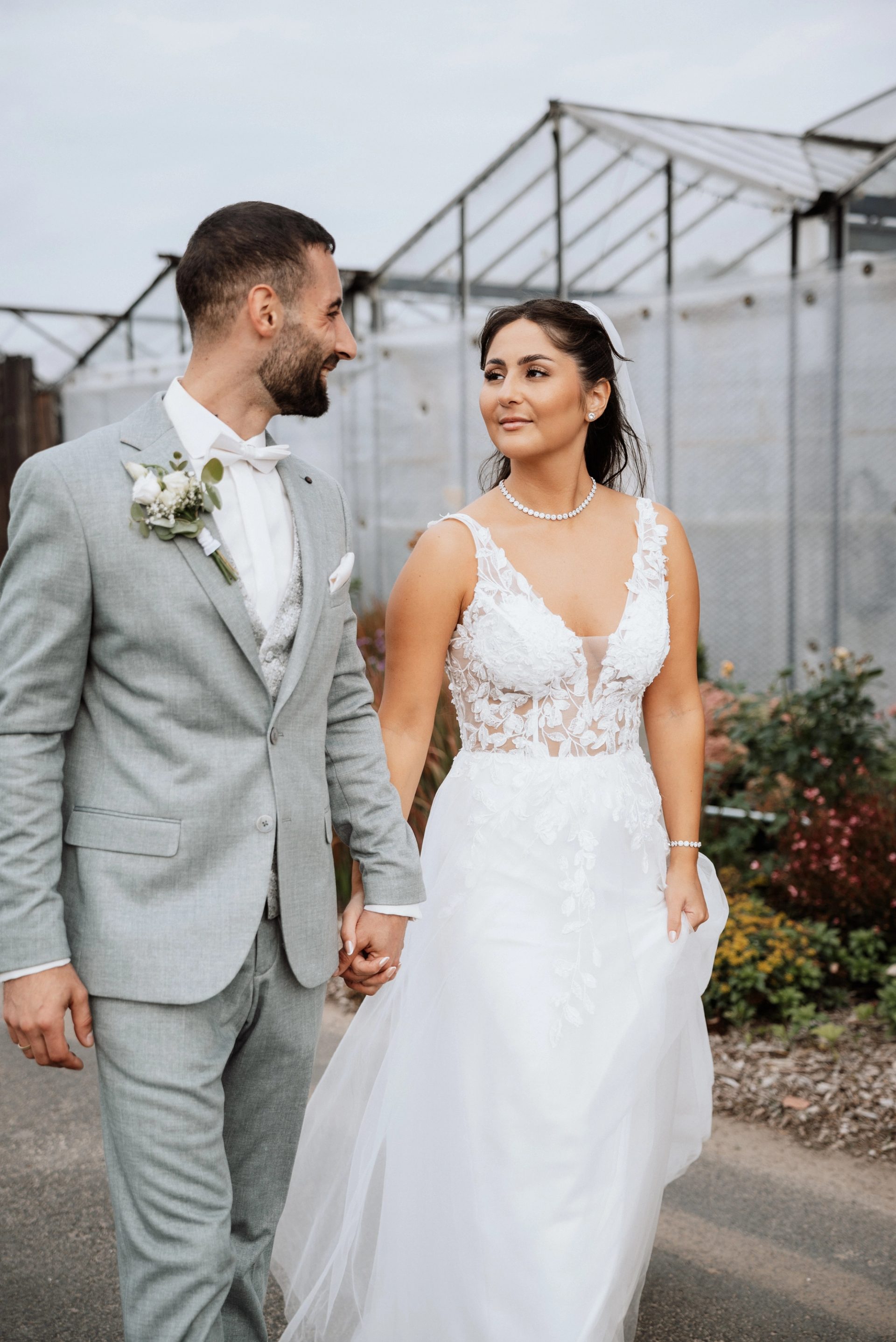 Merve und Timur spazieren Hand in Hand an Blumenbeeten vorbei