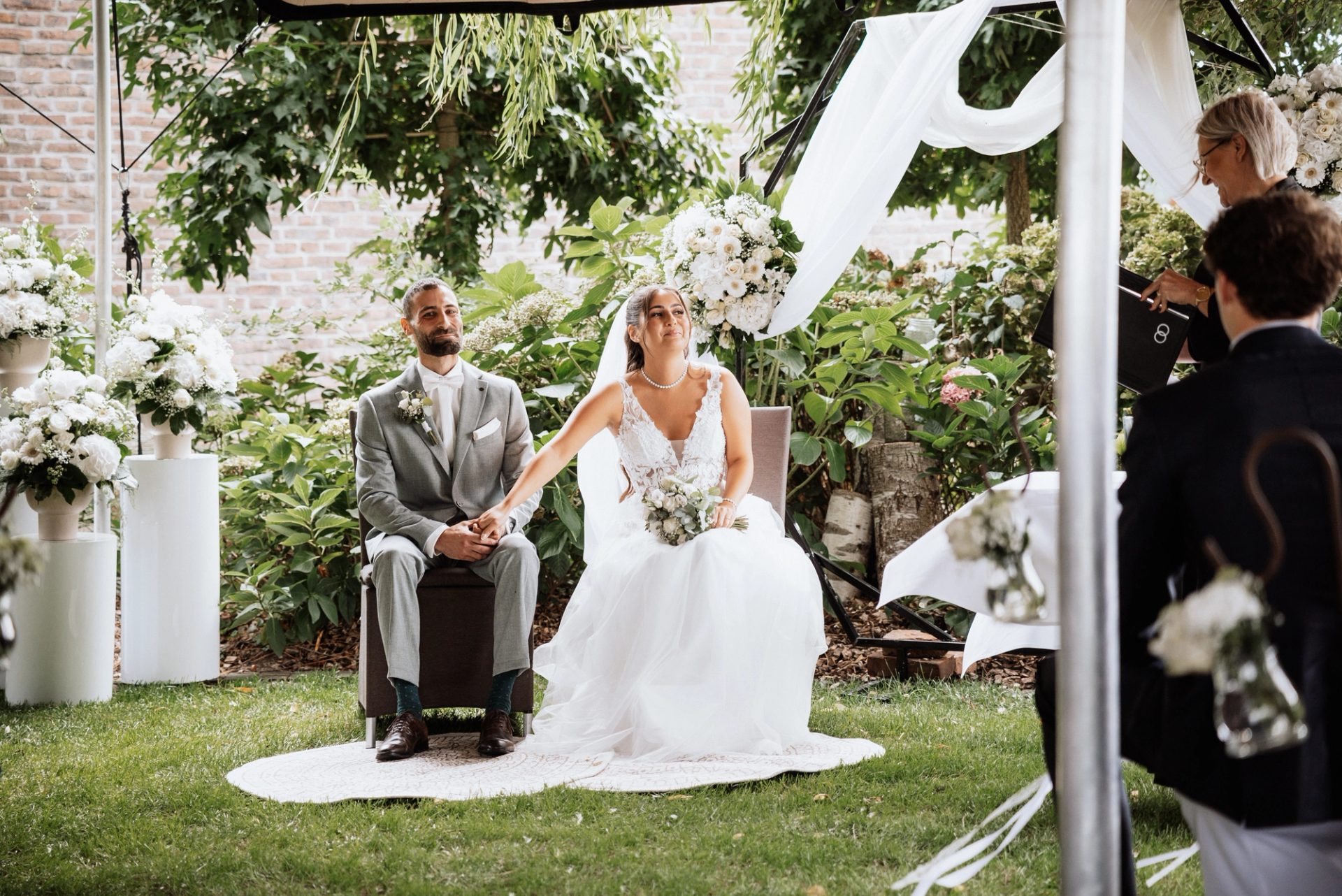 Freie Trauung im Garten des Festsaals Permeshof: Merve und Timur sitzen vor dem Blumenbogen