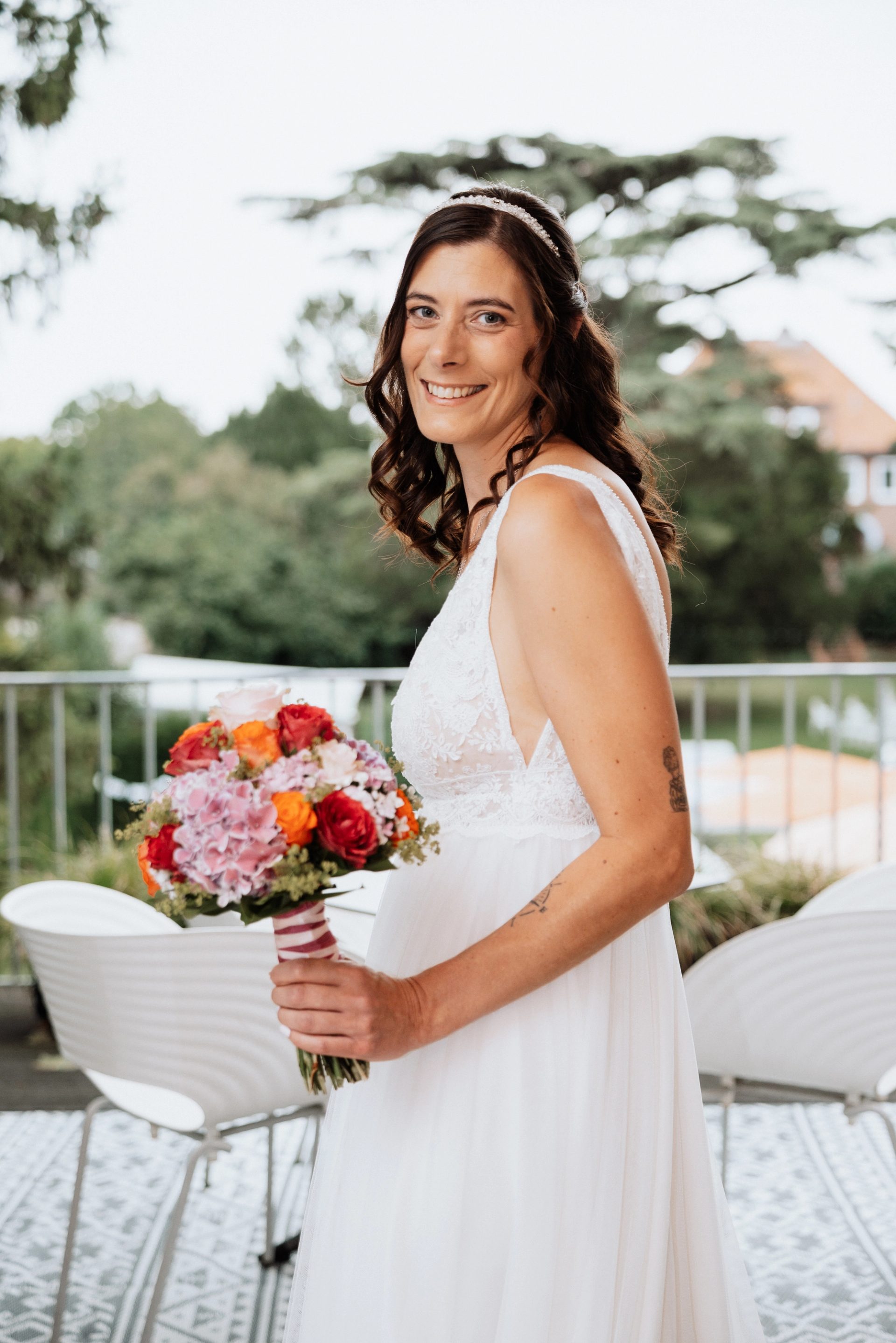 Maren mit Brautstrauß und Haarreif lächelt auf der Terrasse der Villa Glanzstoff