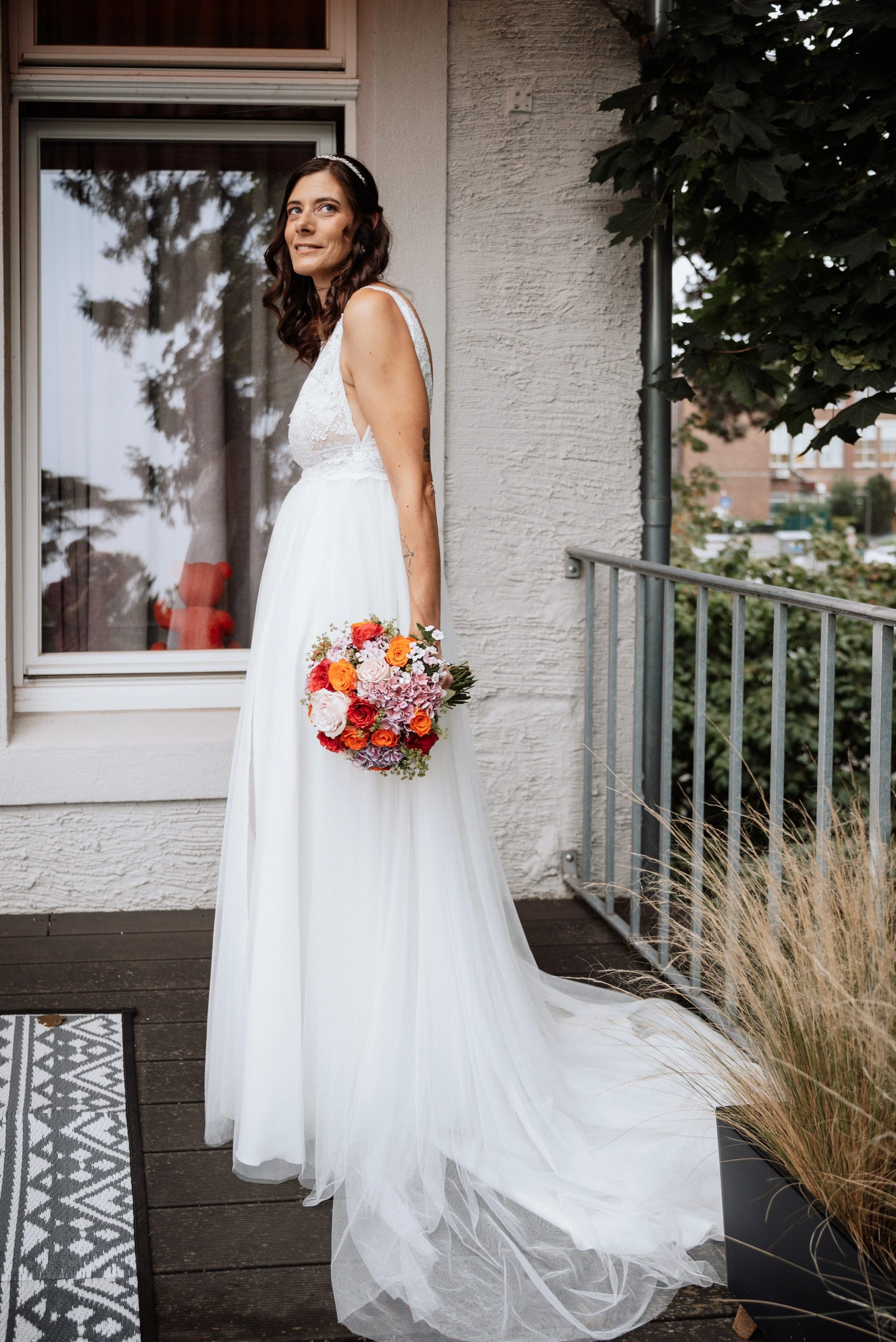 Maren im Brautkleid steht mit dem Strauß an einem Fenster der Villa Glanzstoff und schaut zur Seite