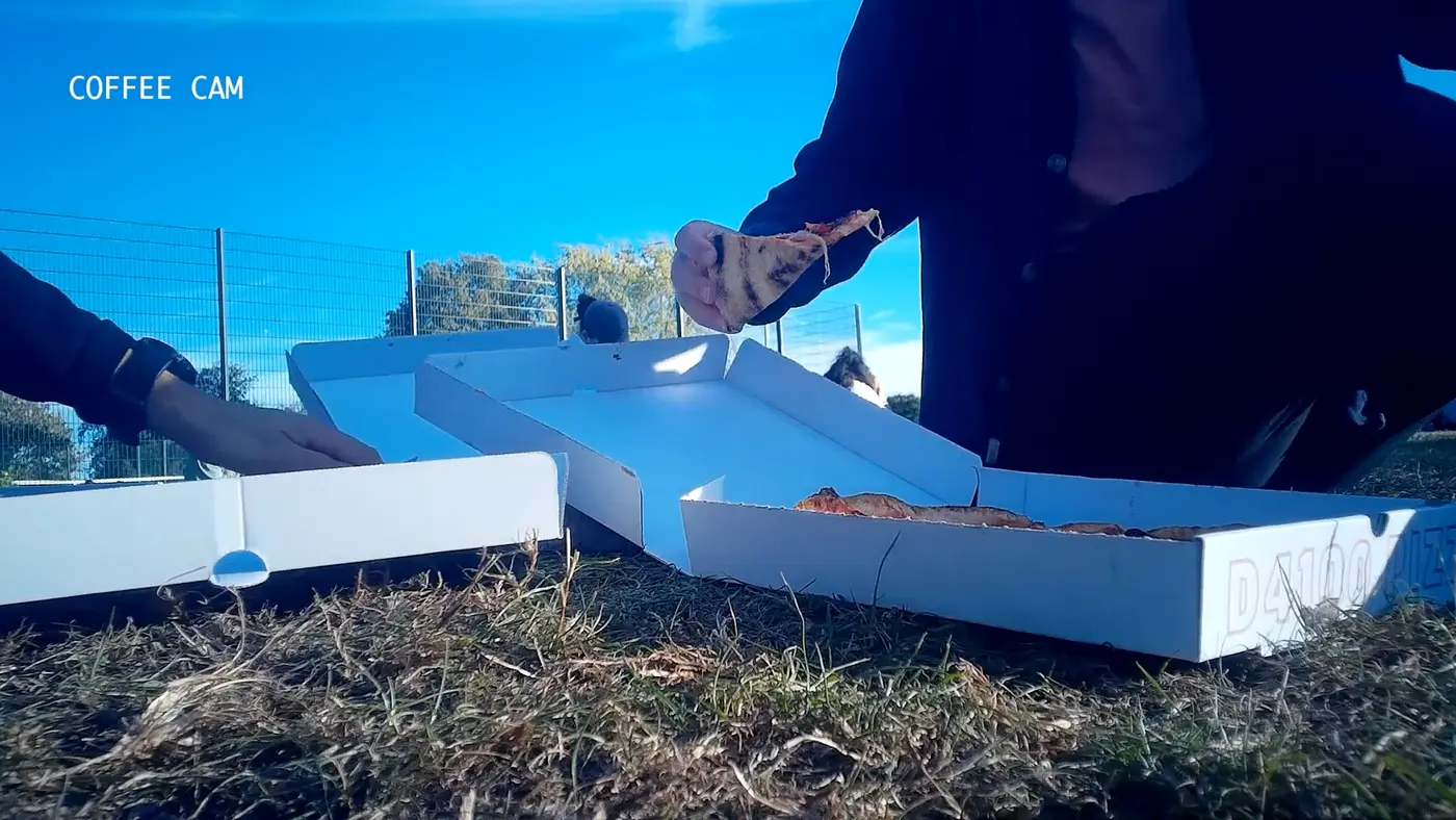 A frame from the hidden coffee cup camera, with a pizza box open on the grass