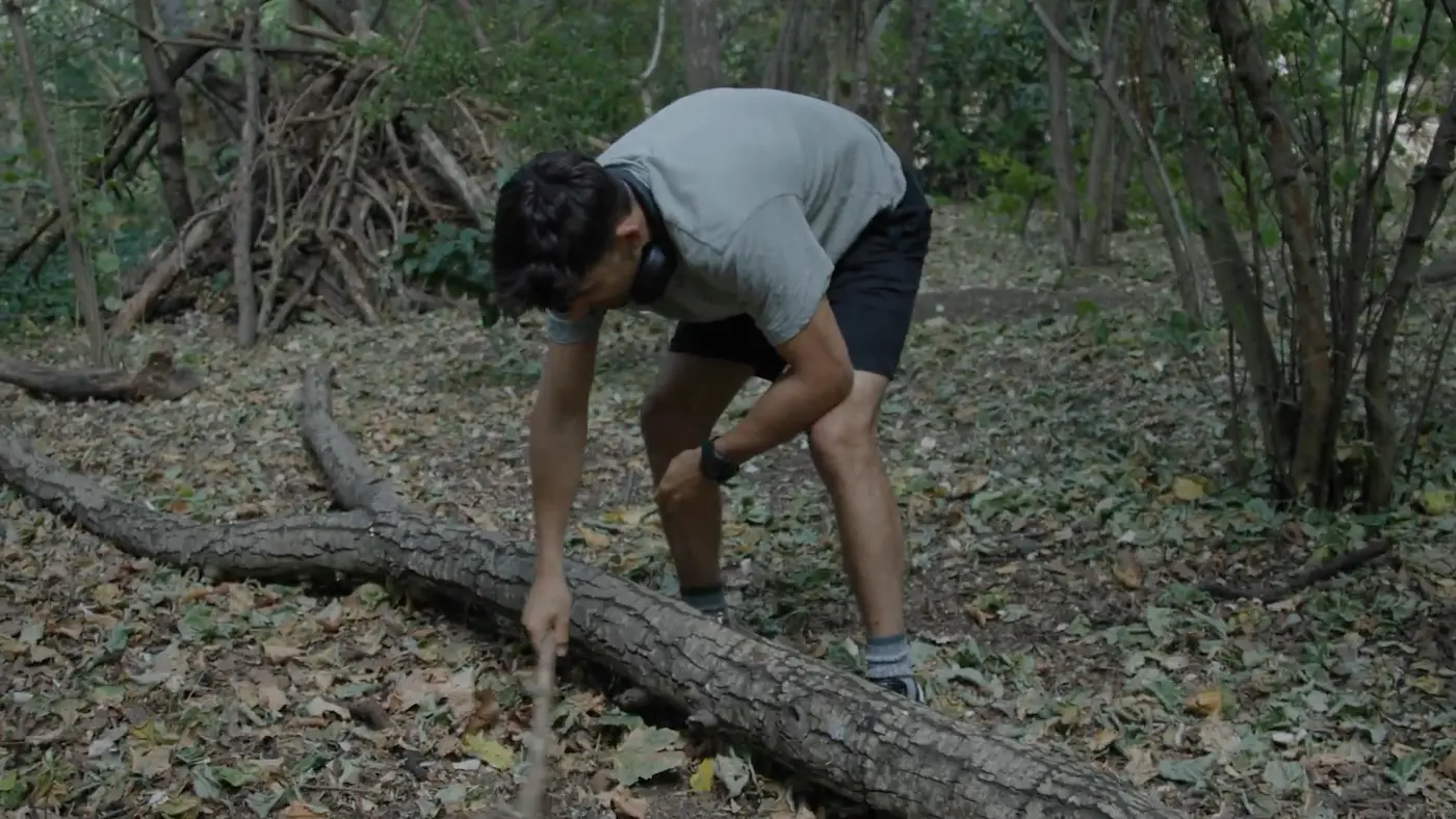 Ben digging a hole with a stick in the woods to bury the box