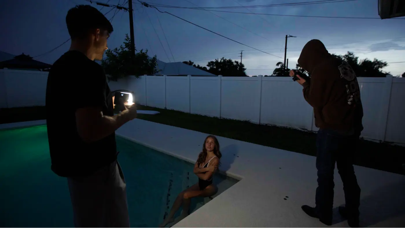 Ben lighting a shot of Anya in her pool at dusk while Hoodie Guy films