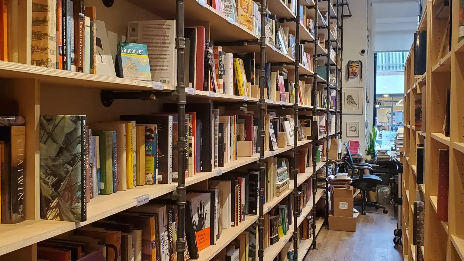 The interor of Massy Books in Vancouver. Tall pipe and wood shelves stretch toward a high ceiling.