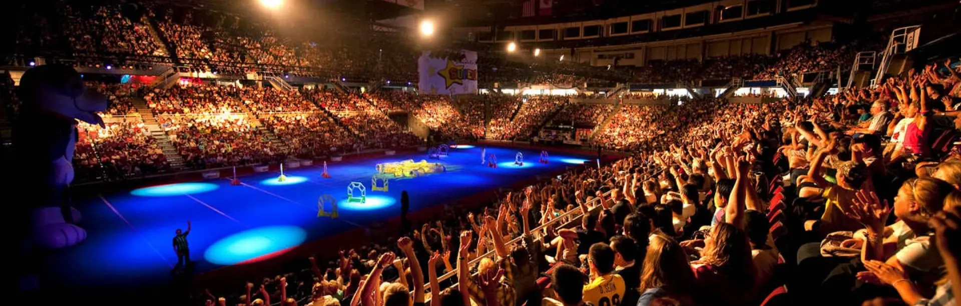 A crowd of cheering fans at an indoor stadium with blue spotlights shining.