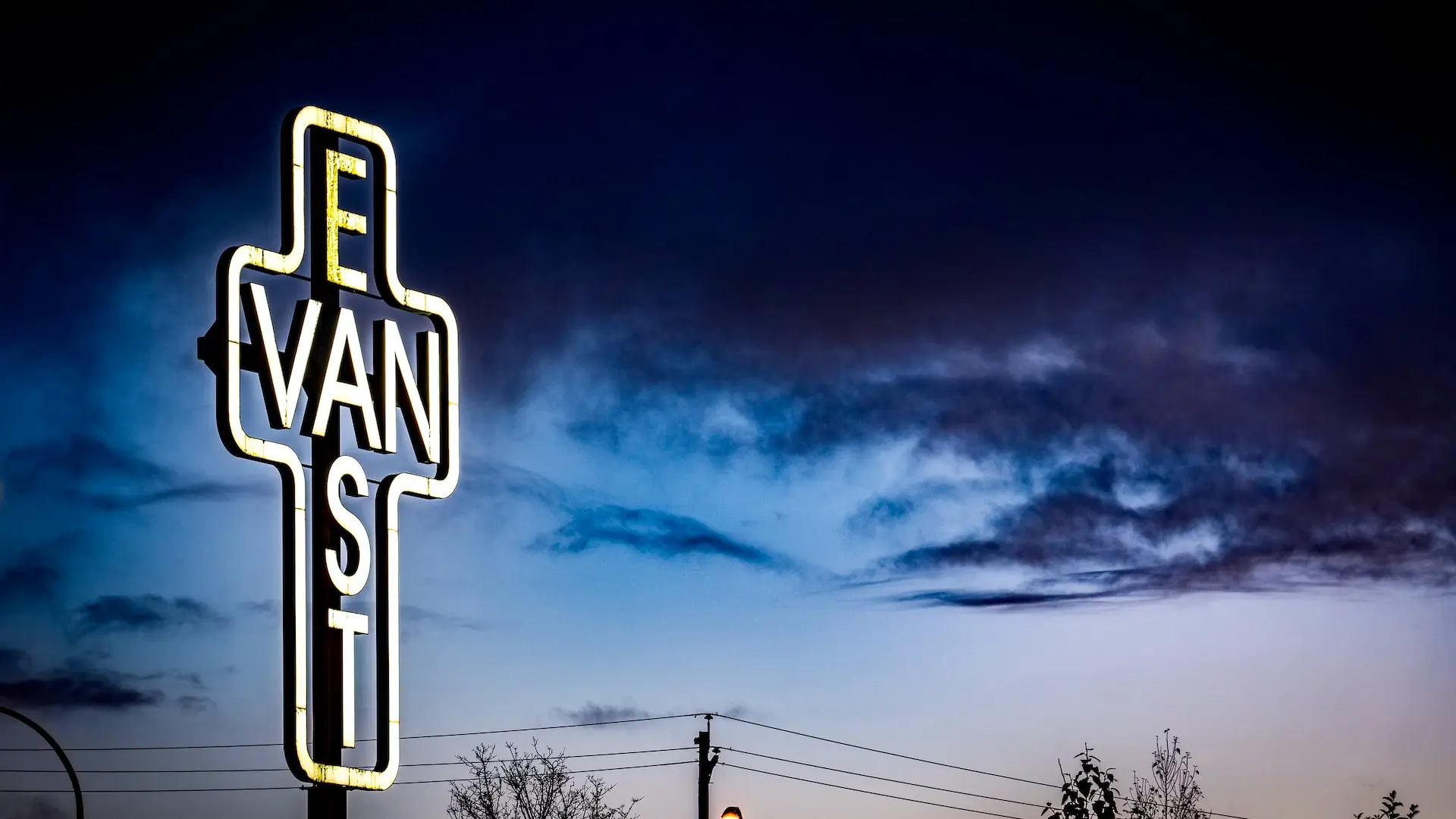 An illuminated cross with the words East Van against the night sky.
