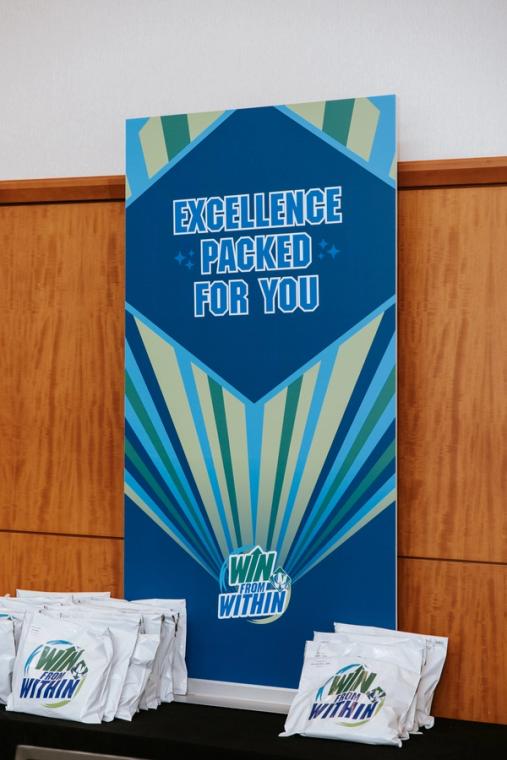 Excellence Packed For You roll-up banner beside branded tote bags