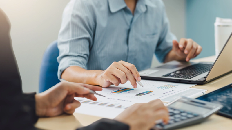 Small business owners reviewing their cash flow while using a laptop and a calculator.