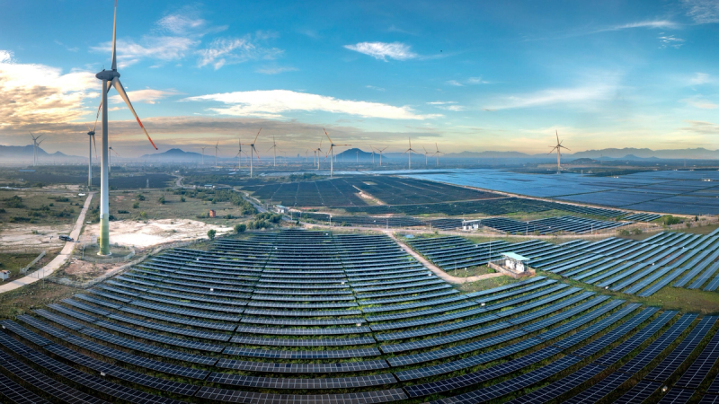 Aerial view of a large solar panel farm alongside wind turbines in a rural landscape.