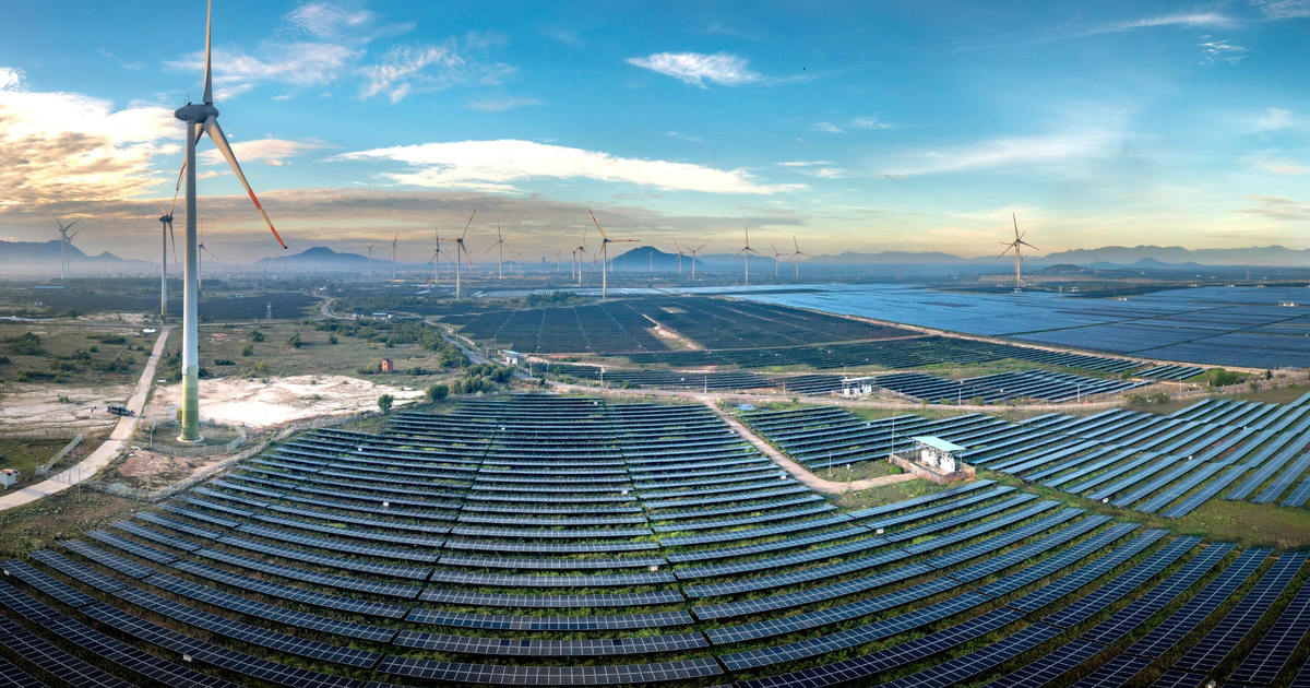 Aerial view of a large solar panel farm alongside wind turbines in a rural landscape.