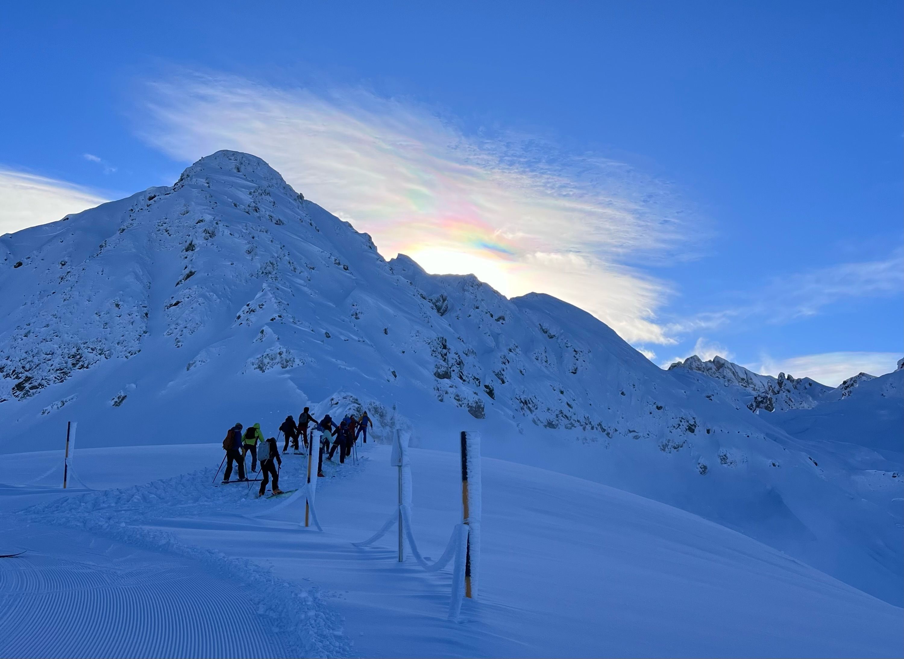 Skiing past a snow-covered mountain under a blue sky with high clouds