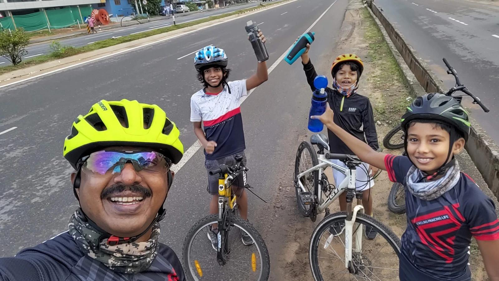 Young riders raising water bottles beside their bicycles with an adult cyclist.