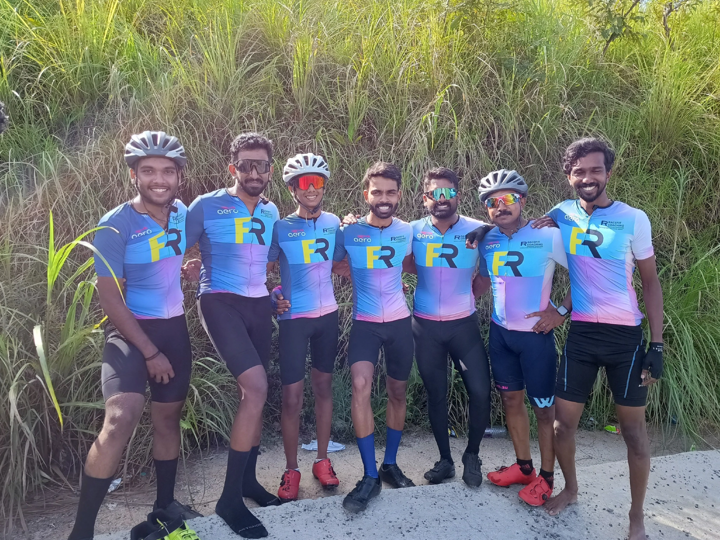 Seven RaceFit cyclists, including Juan Joy and Saiju DS, posing together in their cycling jerseys during a group ride to Illikkal Kallu.
