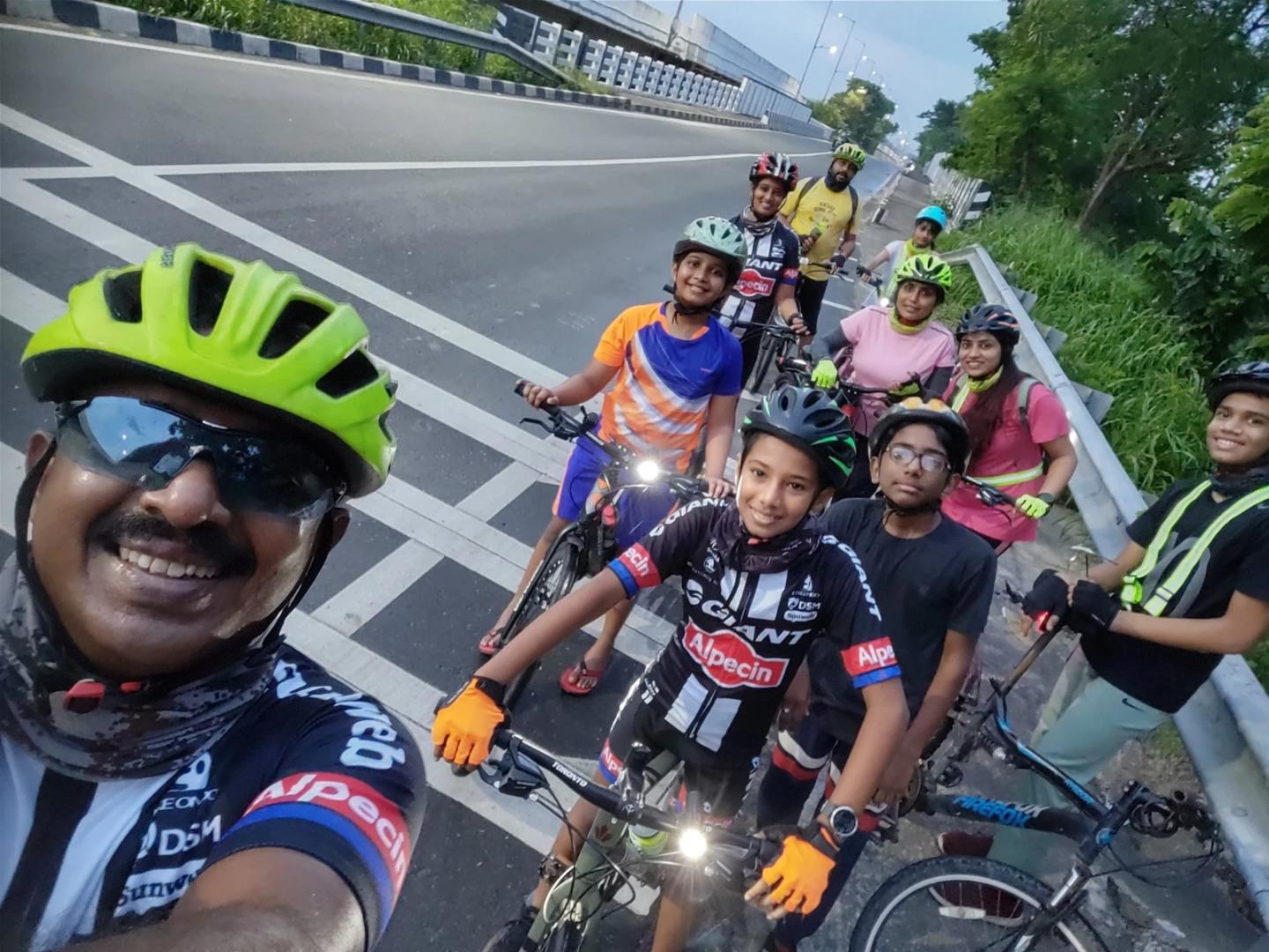 A growing group of children and adults with bicycles beside the road.