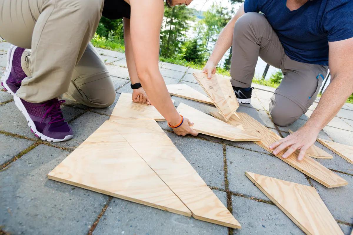 Grupa osób na zewnątrz układa duże drewniane elementy przypominające puzzle