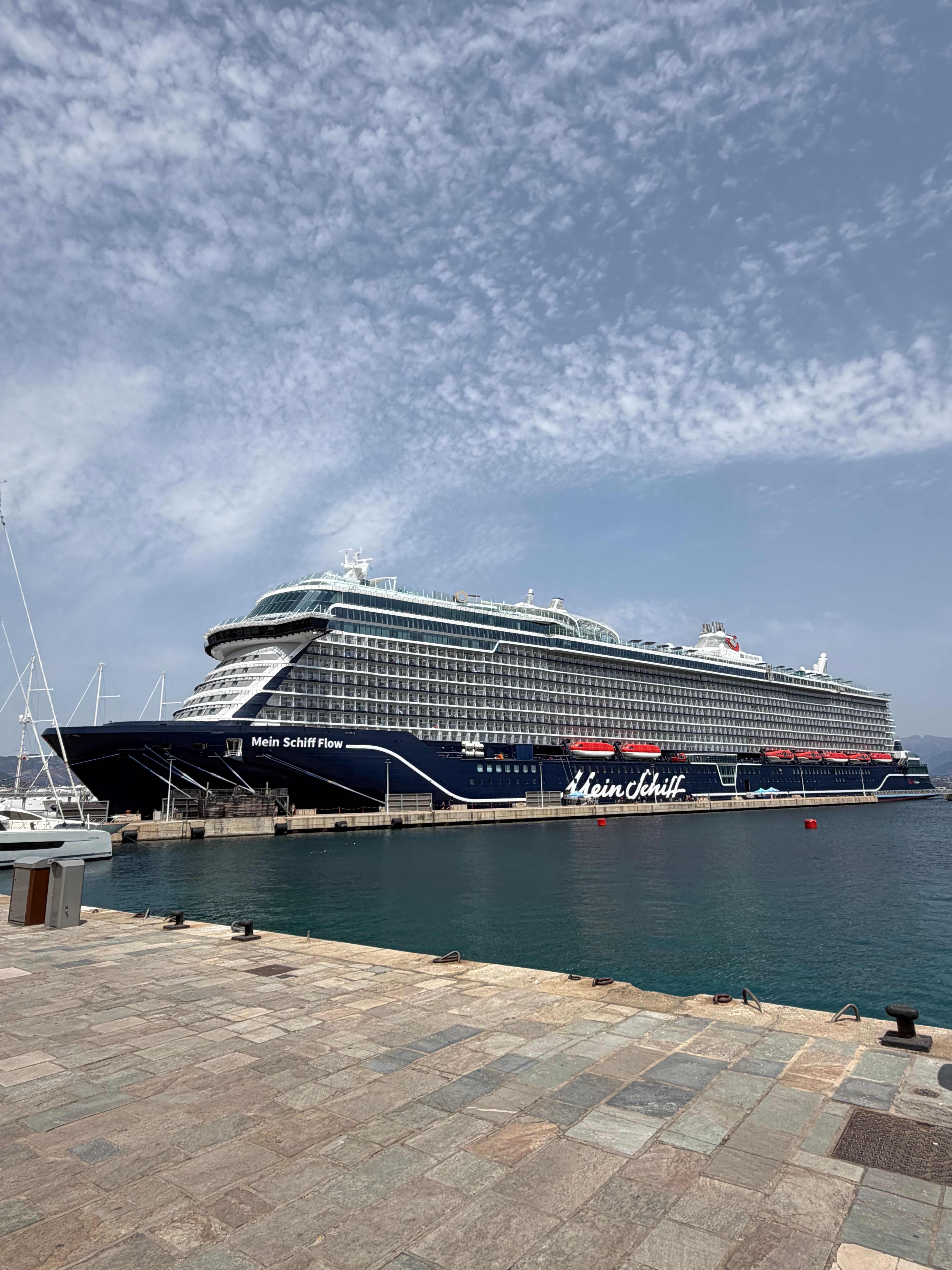 A majestic cruise ship docked at Ajaccio harbor under a partly cloudy sky.