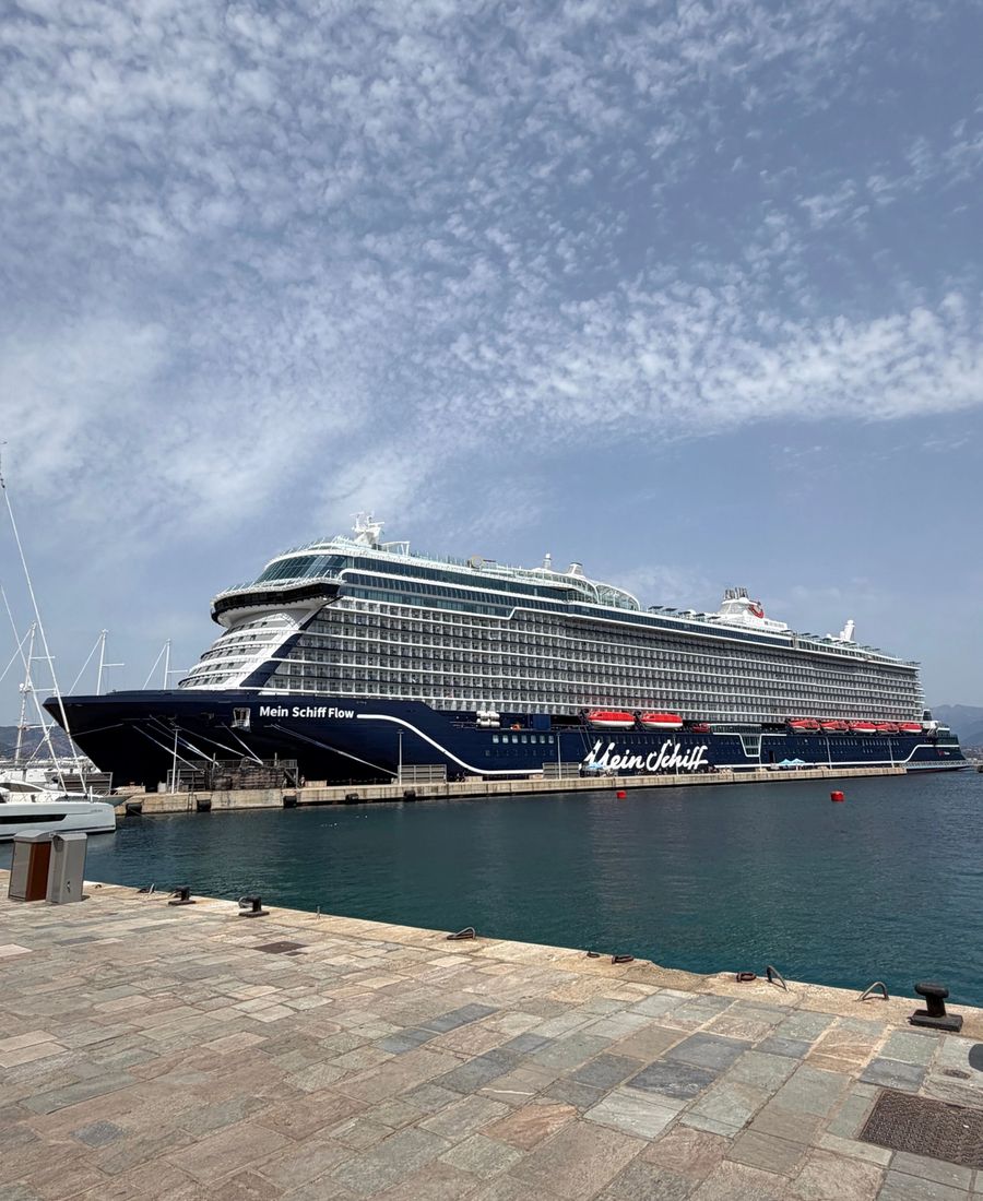 A majestic cruise ship docked at Ajaccio harbor under a partly cloudy sky.