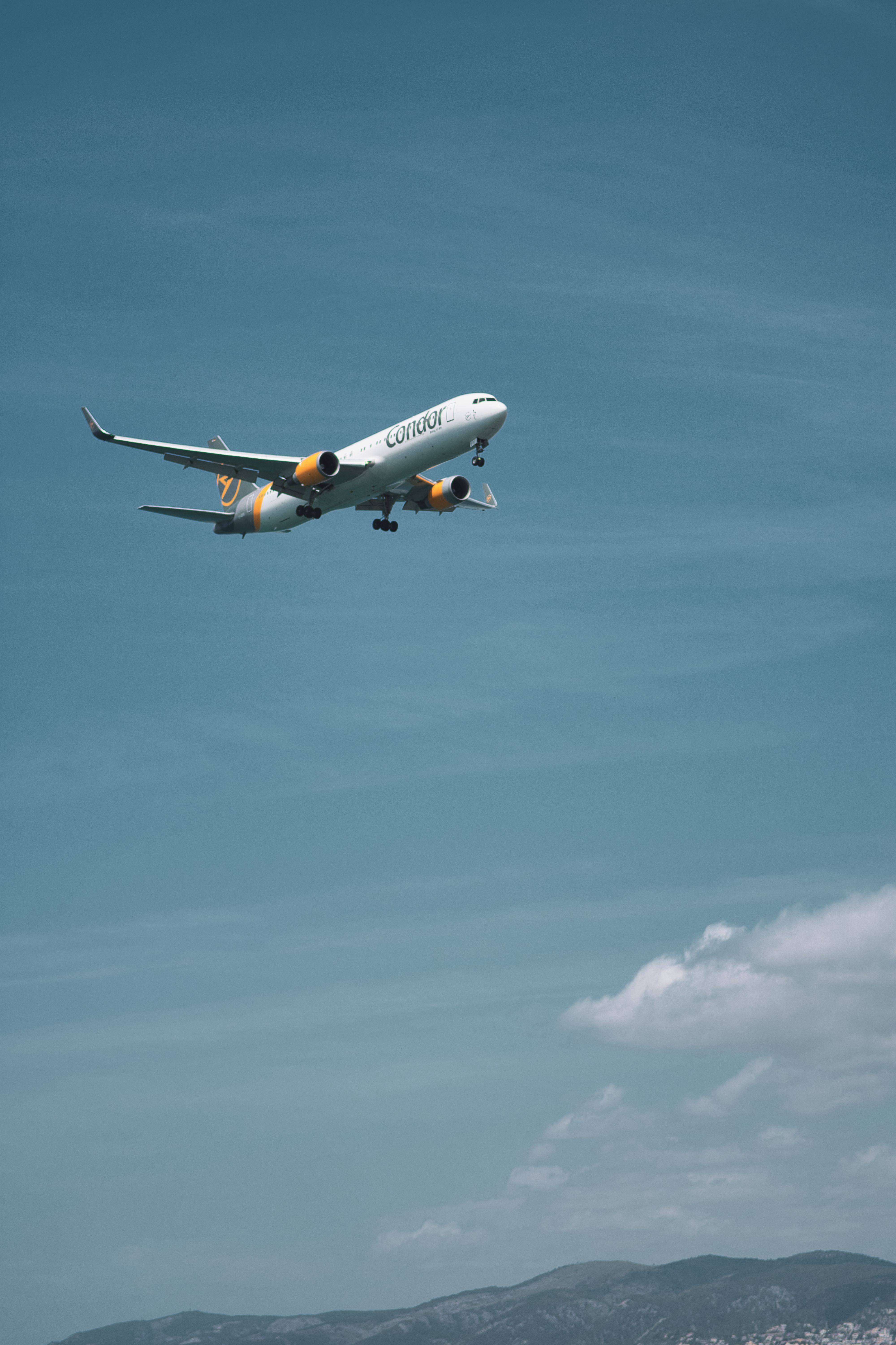 A passenger airplane flying against a backdrop of a clear blue sky and distant mountains.