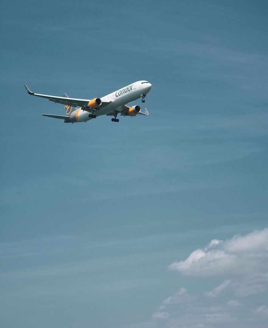 A passenger airplane flying against a backdrop of a clear blue sky and distant mountains.