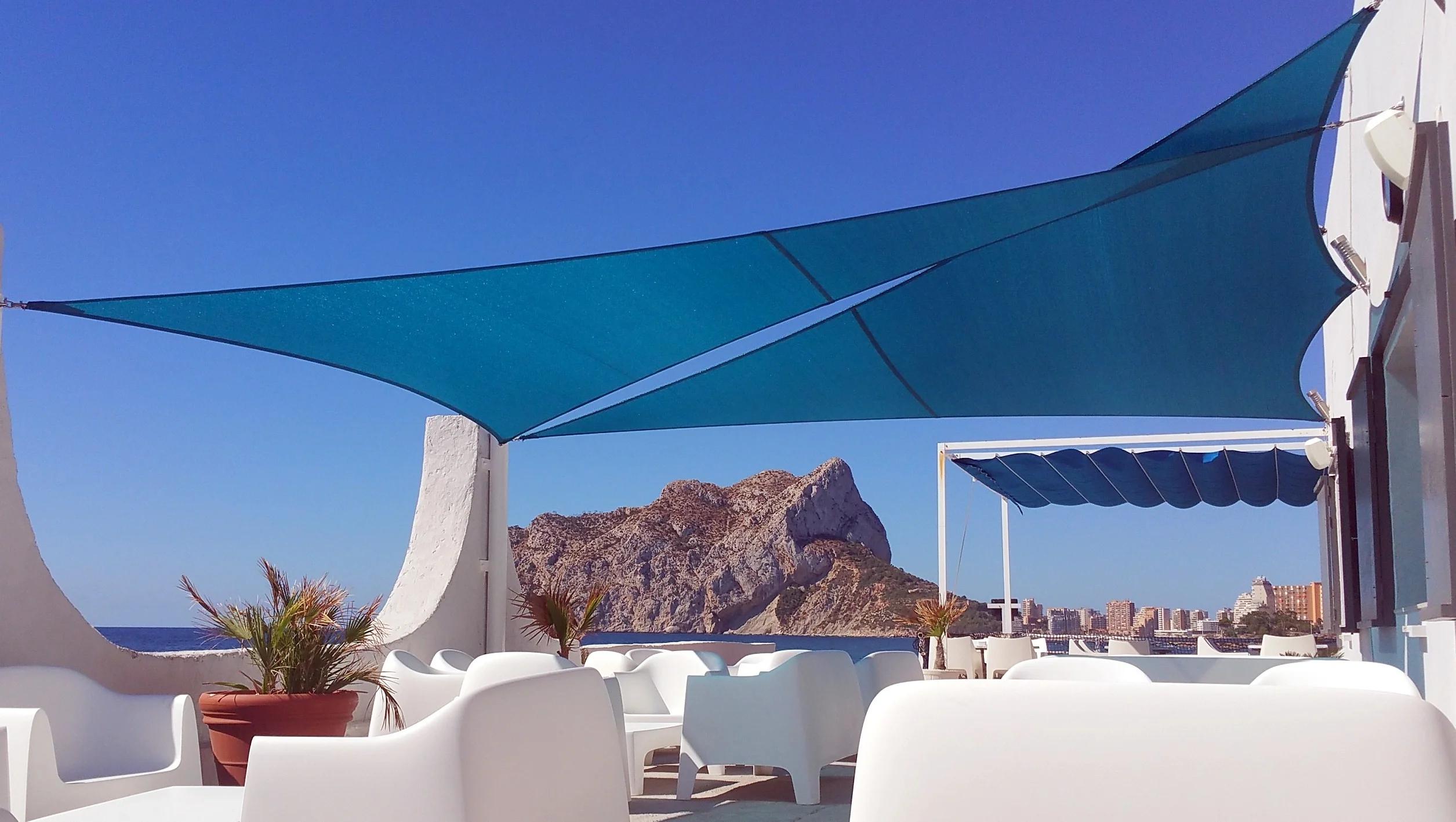 Blauwe maatwerk schaduwdoeken boven een terras aan zee met uitzicht op de Penon de Ifach