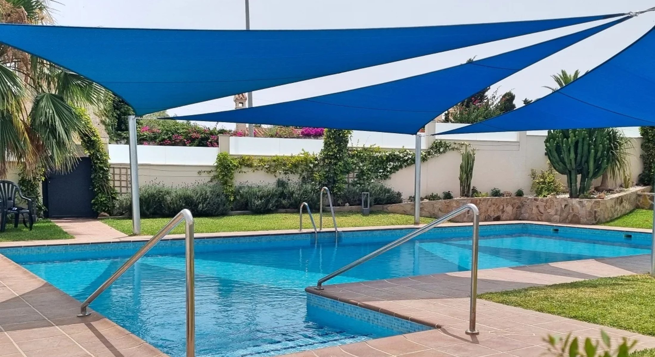Blue triangular shade sails installed above a private swimming pool garden