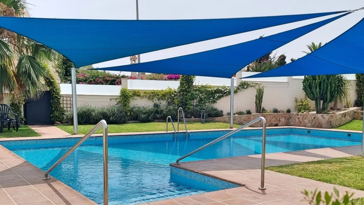 Blue triangular shade sails installed above a private swimming pool garden