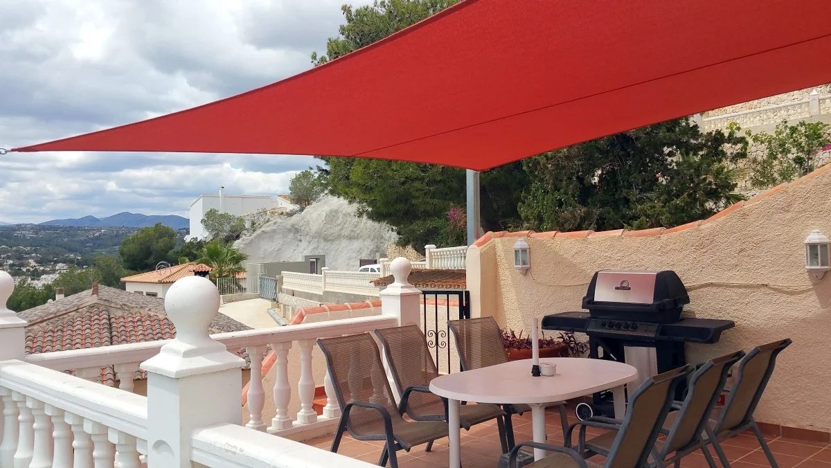 Red triangular shade sail installed above a terrace dining area with mountain views